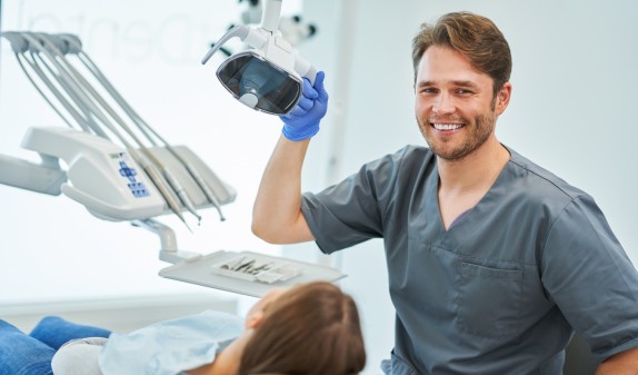 Zahnarzt lächelt neben Patientin auf dem Behandlungsstuhl